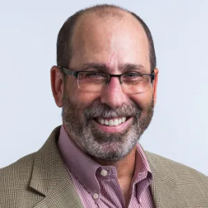 Portrait of smiling man with a beard wearing eyeglasses, pink button up shirt with tan sport jacket.