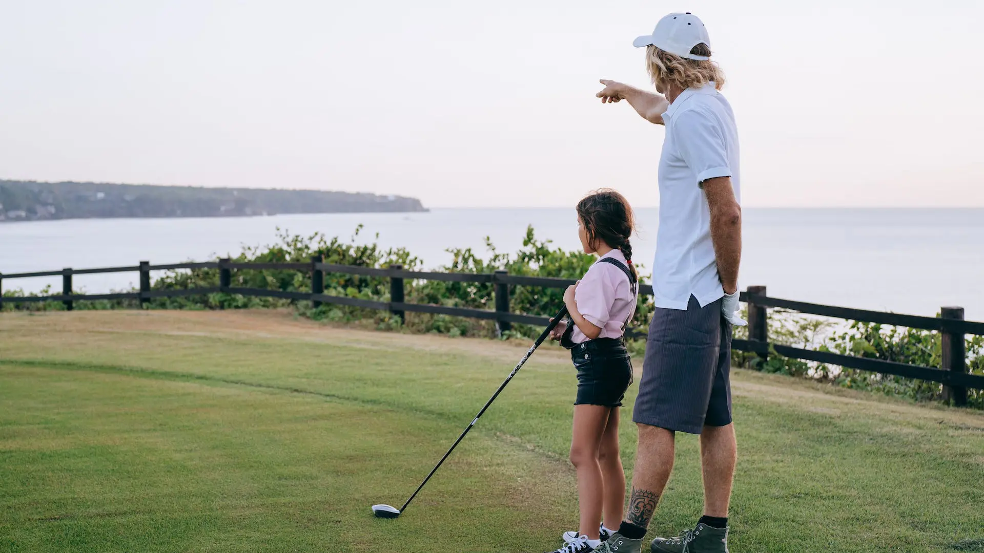 Golf instructors with white polo shirt showing a young girl student golfer where to hit the golf ball