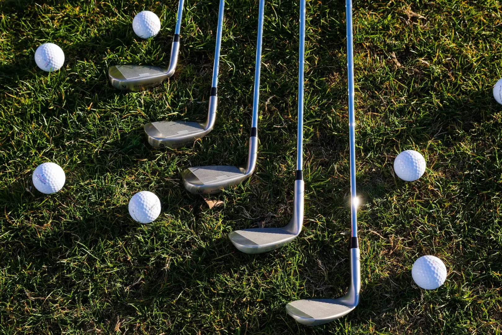 silver golf clubs and golf balls flat on grass